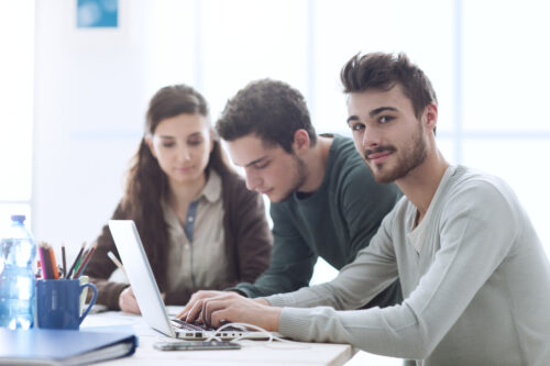 Group of college students at desk using a laptop, networking and studying together, education and learning concept